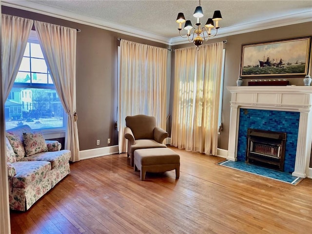 sitting room with a textured ceiling, a tile fireplace, crown molding, wood finished floors, and an inviting chandelier