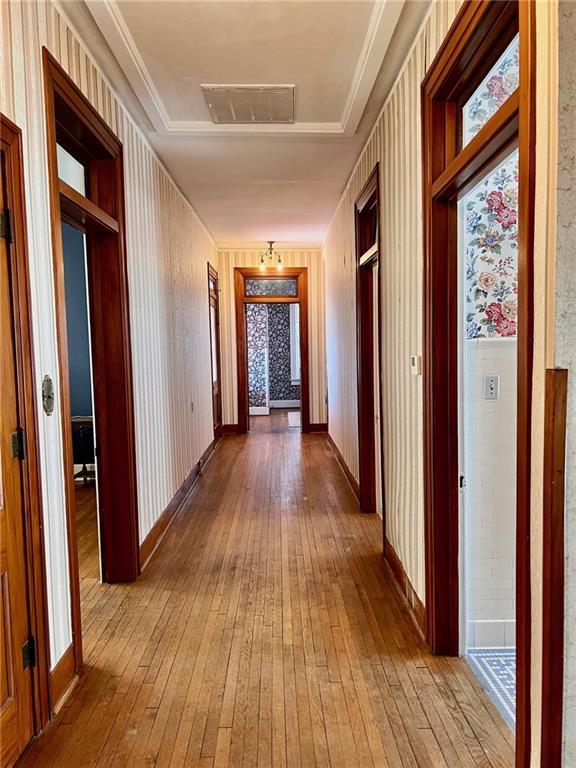 hall with wood finished floors, visible vents, and baseboards