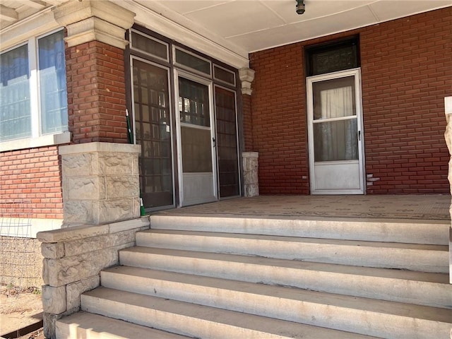 doorway to property with a porch and brick siding