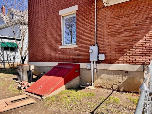 exterior details with a bulkhead entry, brick siding, electric meter, and central air condition unit