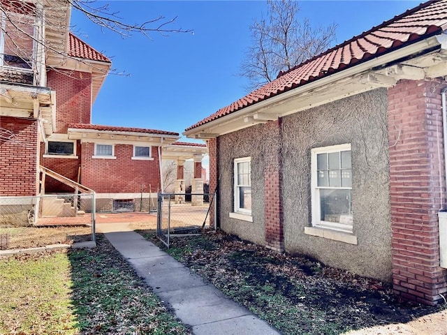 view of home's exterior featuring brick siding, a tile roof, and fence