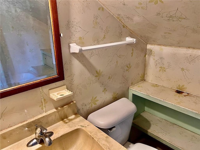 bathroom with a sink, toilet, and wallpapered walls