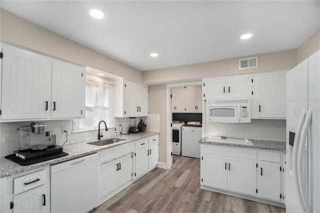 kitchen featuring washer and clothes dryer, visible vents, white cabinets, a sink, and white appliances