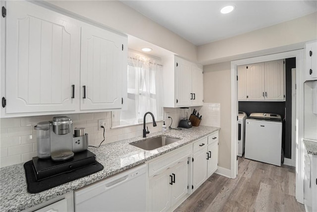 kitchen with dishwasher, light wood-style floors, washing machine and dryer, white cabinetry, and a sink