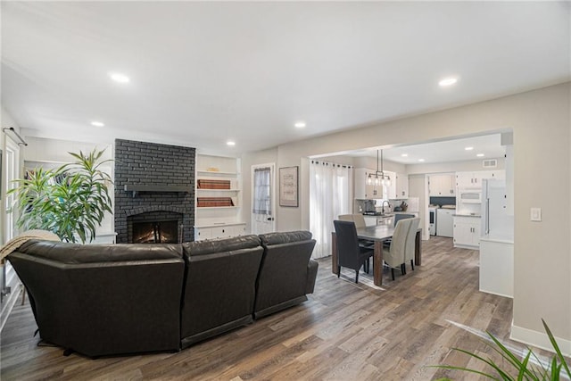 living room with visible vents, baseboards, wood finished floors, a fireplace, and recessed lighting