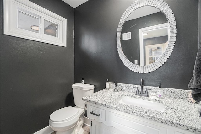 half bathroom with baseboards, vanity, and toilet