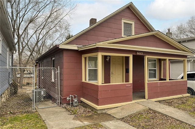 bungalow with covered porch, a chimney, fence, and a gate