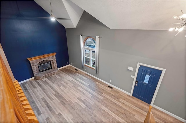 interior space with a brick fireplace, baseboards, visible vents, and wood finished floors