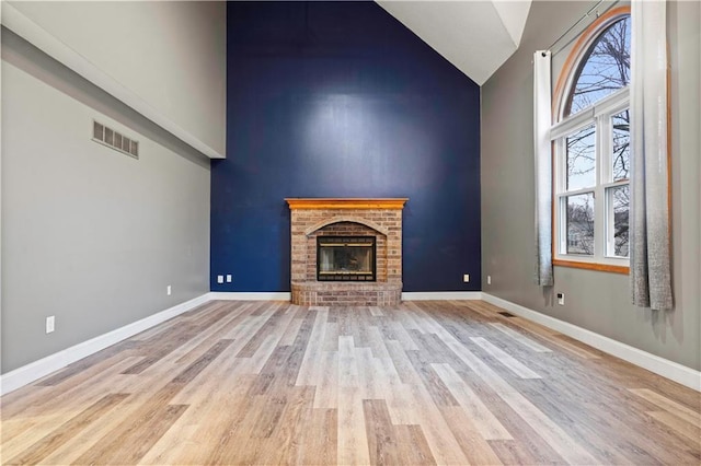 unfurnished living room with high vaulted ceiling, wood finished floors, visible vents, and baseboards