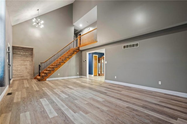 unfurnished living room featuring an inviting chandelier, visible vents, stairway, and wood finished floors