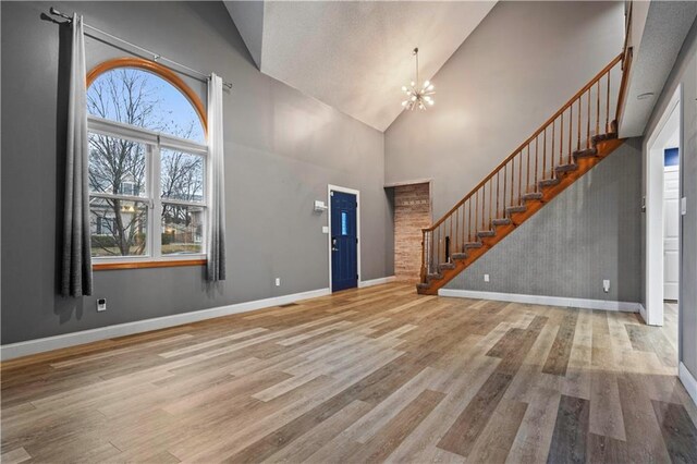 foyer entrance featuring stairs, high vaulted ceiling, wood finished floors, and an inviting chandelier