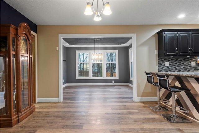 kitchen featuring dark cabinetry, decorative backsplash, light wood-style floors, and a notable chandelier