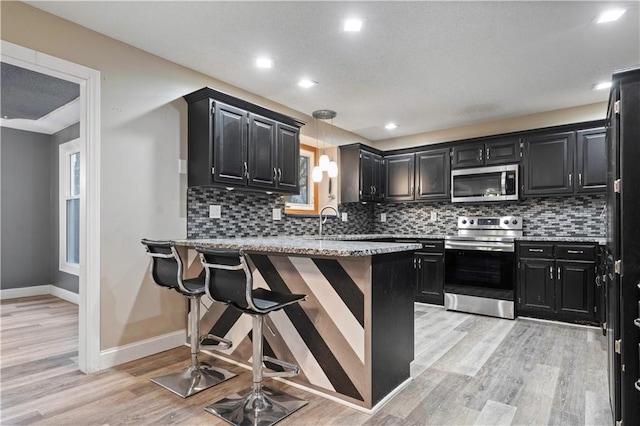 kitchen with light wood-type flooring, a peninsula, appliances with stainless steel finishes, and dark cabinetry