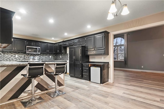 kitchen with tasteful backsplash, stainless steel microwave, light wood-style flooring, dark cabinetry, and baseboards