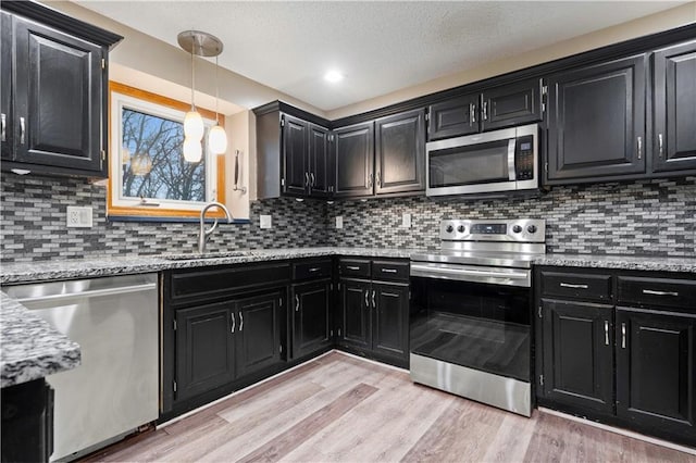 kitchen with a sink, light wood finished floors, appliances with stainless steel finishes, and dark cabinets