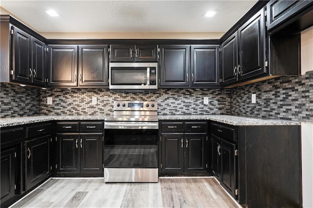 kitchen featuring stainless steel appliances, light wood-type flooring, and dark cabinets