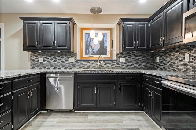 kitchen with stainless steel appliances, light wood-type flooring, dark cabinetry, and a sink