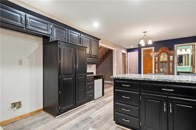 kitchen featuring baseboards, light wood-style floors, an inviting chandelier, and dark cabinets