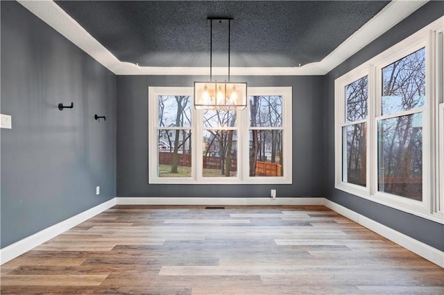 unfurnished dining area with a textured ceiling, a notable chandelier, wood finished floors, and baseboards