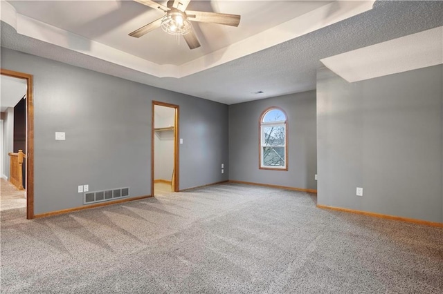 carpeted empty room featuring a ceiling fan, a raised ceiling, visible vents, and baseboards