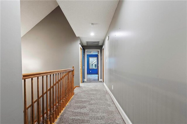 corridor with baseboards, visible vents, an upstairs landing, a textured ceiling, and carpet flooring