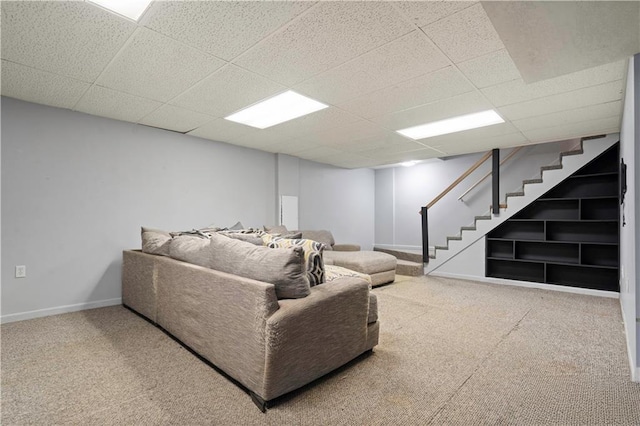 carpeted living area featuring a drop ceiling, baseboards, and stairs