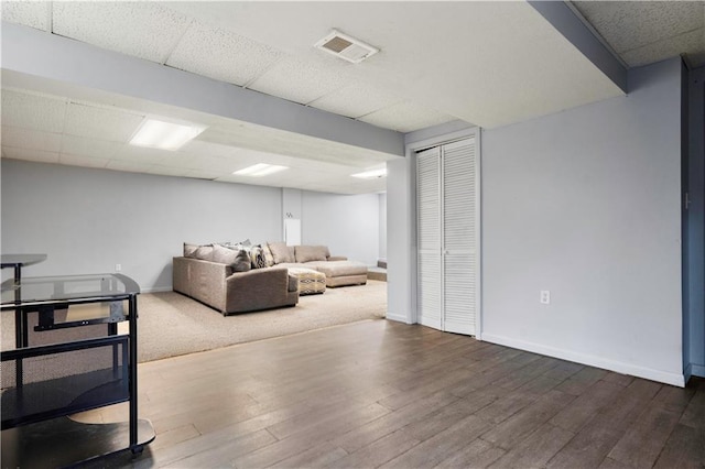 living area with a paneled ceiling, visible vents, baseboards, and wood finished floors