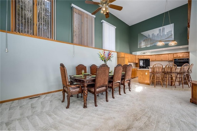 dining room featuring ceiling fan, high vaulted ceiling, baseboards, and light carpet