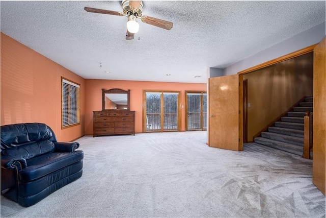 living area featuring carpet flooring, a textured ceiling, ceiling fan, and stairs