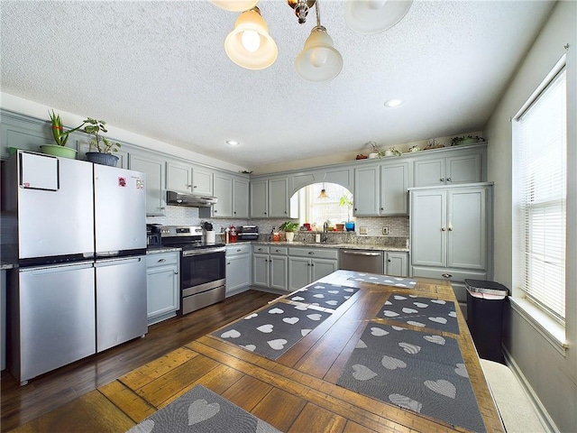 kitchen with under cabinet range hood, gray cabinets, stainless steel appliances, and a wealth of natural light