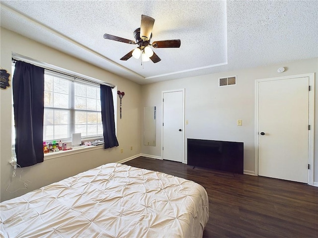 bedroom with visible vents, a raised ceiling, ceiling fan, dark wood-style flooring, and a textured ceiling