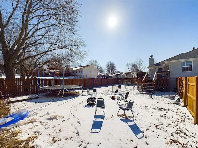 yard layered in snow with a trampoline, a residential view, fence, and stairway