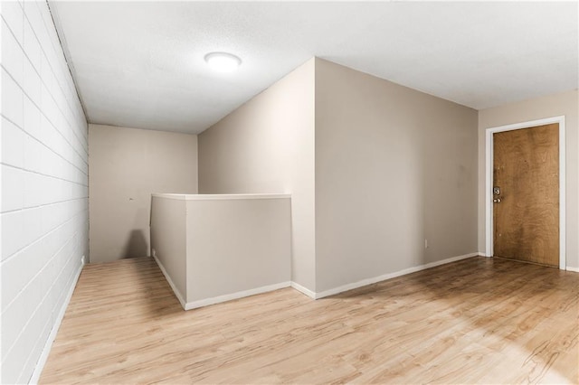 hallway featuring concrete block wall, light wood-style flooring, and an upstairs landing