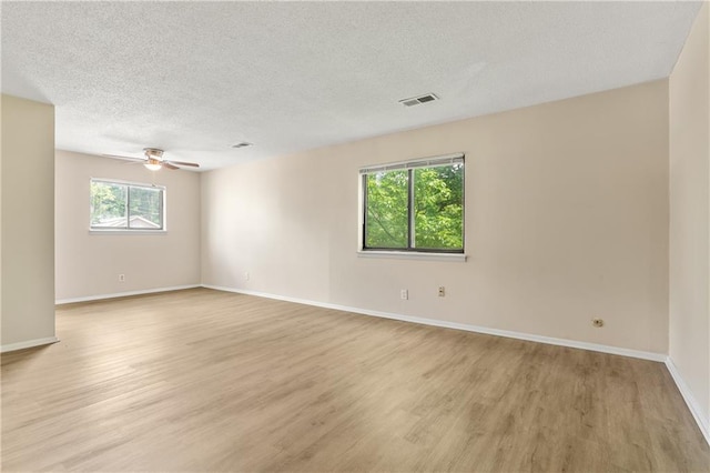 spare room featuring visible vents, baseboards, light wood-style flooring, and a textured ceiling