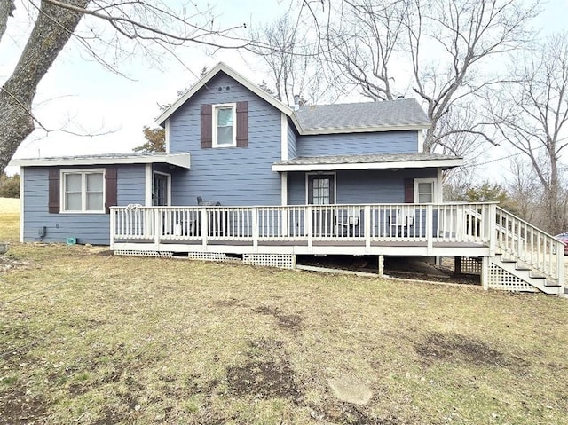 view of front facade with roof with shingles, a wooden deck, and a front lawn