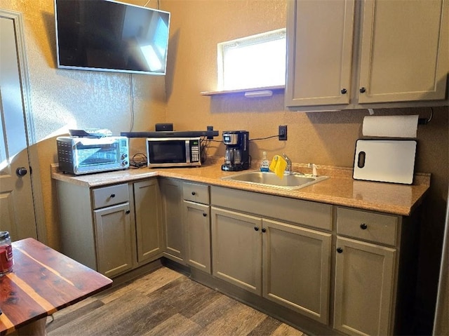 kitchen featuring dark wood-style floors, stainless steel microwave, light countertops, gray cabinetry, and a sink