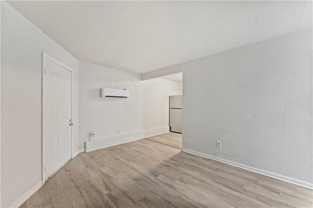 spare room with light wood-type flooring, baseboards, and a wall mounted AC