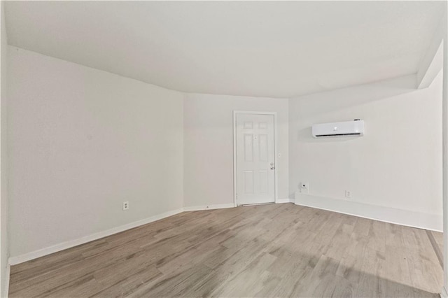 unfurnished room with a wall mounted AC, light wood-style flooring, and baseboards