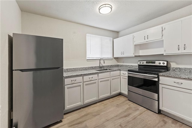 kitchen with a textured ceiling, light wood-style flooring, stainless steel appliances, a sink, and white cabinetry