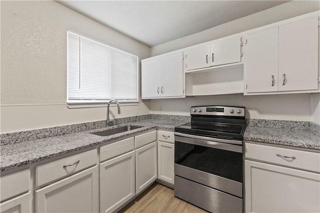 kitchen with light stone counters, under cabinet range hood, a sink, white cabinets, and stainless steel electric range