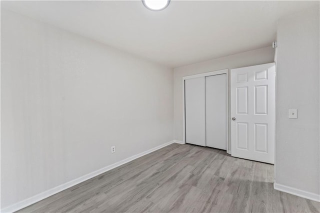 unfurnished bedroom with a closet, light wood-style flooring, and baseboards