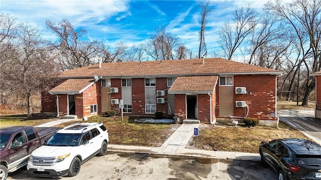 view of property featuring uncovered parking, brick siding, and a shingled roof