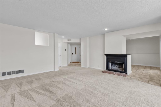 unfurnished living room with carpet floors, visible vents, a fireplace with raised hearth, and baseboards