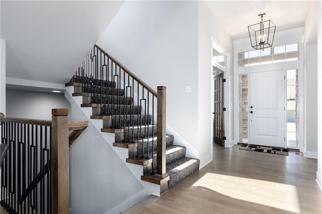 entrance foyer with a notable chandelier, wood finished floors, stairway, baseboards, and a towering ceiling