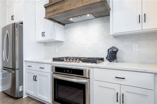 kitchen with light stone counters, decorative backsplash, custom range hood, white cabinets, and appliances with stainless steel finishes