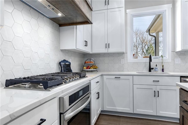 kitchen with a sink, light stone counters, backsplash, white cabinetry, and stainless steel appliances