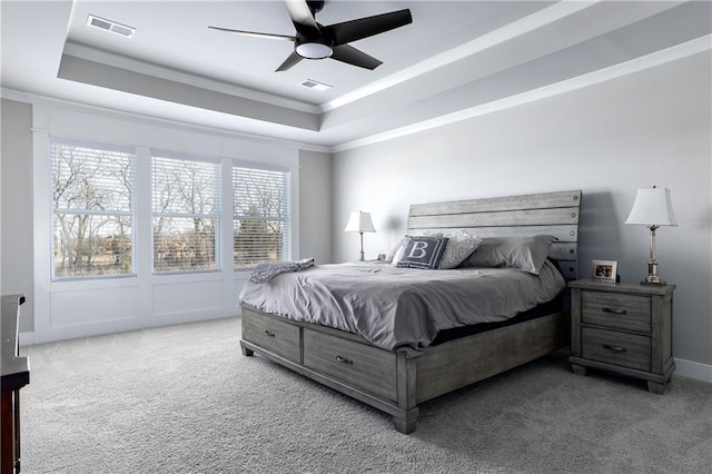 carpeted bedroom with a ceiling fan, a tray ceiling, crown molding, and visible vents