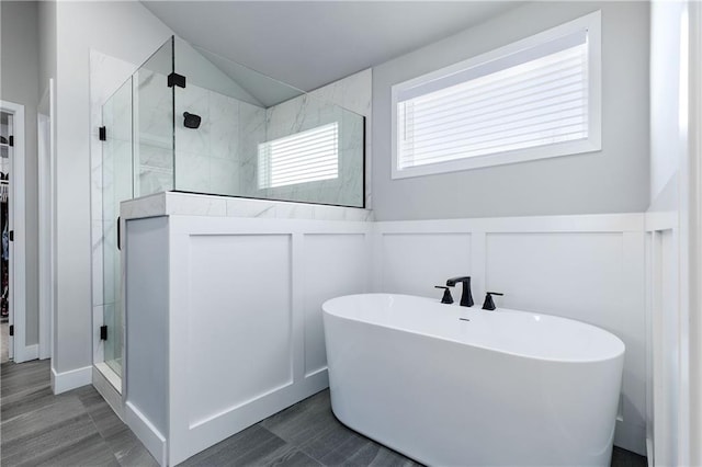 full bath with a wainscoted wall, a freestanding tub, a shower stall, a walk in closet, and a decorative wall