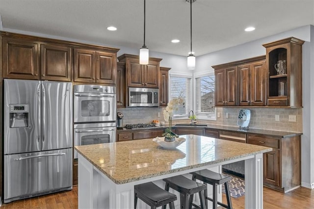 kitchen featuring open shelves, a sink, wood finished floors, stainless steel appliances, and light stone countertops