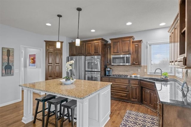 kitchen with light stone countertops, appliances with stainless steel finishes, wood finished floors, and a sink